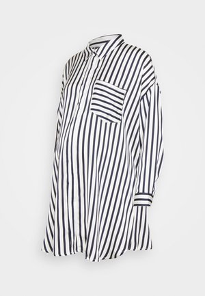 Camisa de maternidad de manga larga con rayas verticales en blanco y negro, cierre frontal con botones y un bolsillo en el pecho con rayas horizontales.