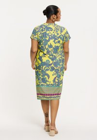 Kleid in Knielänge aus gelbem Stoff, mit blauen floralem und Paisley-Mustern, einem gemusterten Saum und kurzen Ärmeln.