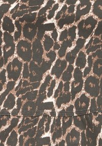 Gros plan sur un tissu avec un motif animalier brun foncé et des taches irrégulières de couleur fauve plus claire, montrant un détail de couture visible.