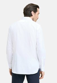 Camicia bianca a maniche lunghe con colletto classico, vestibilità su misura, pince posteriori per una maggiore struttura e polsini con un bottone. Tessuto dalla texture liscia.