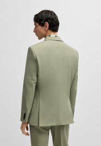 Lys grøn blazer med en skræddersyet pasform, glat tekstur, spidse klapper og en enkelt slids. Har sorte knapper på manchetterne.