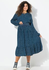 Mekko, jossa on tummansinisiä valkoisia pilkkuja, pitkät hihat, kiristettävä kaula-aukko, kapeat vyötärö ja kerroksellinen hameosa. Yhdistetty tummansineisiin urheilujalkineisiin.