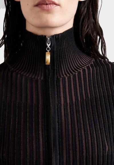 Juoda grubi zip-up palaidinė su aukštu apykakle. Ypatumai: sidabrinė užtrauktuko detalė su kreminės spalvos traukimo juostele, pabrėžianti tekstūrą ir detales.