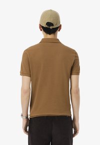 Brun kortärmad polo skjorta med mjuk textur och krage, ihop med en beige keps. Enkel, ren design, sedd bakifrån.