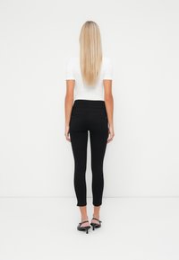 Fekete, slim fit leggingek magas derékkal, rugalmas anyagból készült. Feszes fehér toppal és fekete magassarkúval viselve.