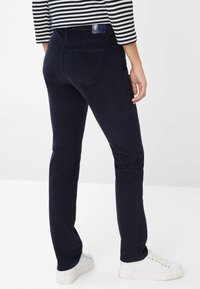 Navy ribcord broek met een aansluitende pasvorm, achterzakken en een klein merkembleem bij de tailleband, gecombineerd met witte sneakers.