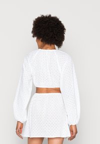 Top cropped branco com bordado perfurado e mangas bufantes longas, combinado com uma saia à condizer; apresenta bordado texturizado e detalhe de cintura elástica.