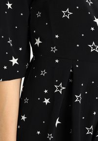 Vestido negro con un tejido texturizado, adornado con estrellas plateadas metálicas de diferentes tamaños, que realzan su patrón y diseño.