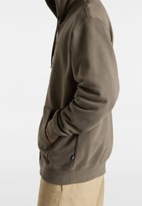 Bluza z kapturem w oliwkowym kolorze, wykonana z miękkiego materiału. Posiada kieszeń typu kangur, ściągacze przy rękawach oraz metkę z logo na dole.