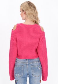 Różowy sweter z dzianiny z ods�łoniętymi ramionami, o prążkowanej fakturze i długich rękawach, w połączeniu z niebieskimi, spranym dżinsami z haftem na kieszeniach.