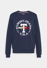 Granatowa bluza z okrągłym dekoltem, ściągaczami przy mankietach i u dołu. Posiada duże haftowane logo z białymi, czerwonymi, złotymi i niebieskimi akcentami.