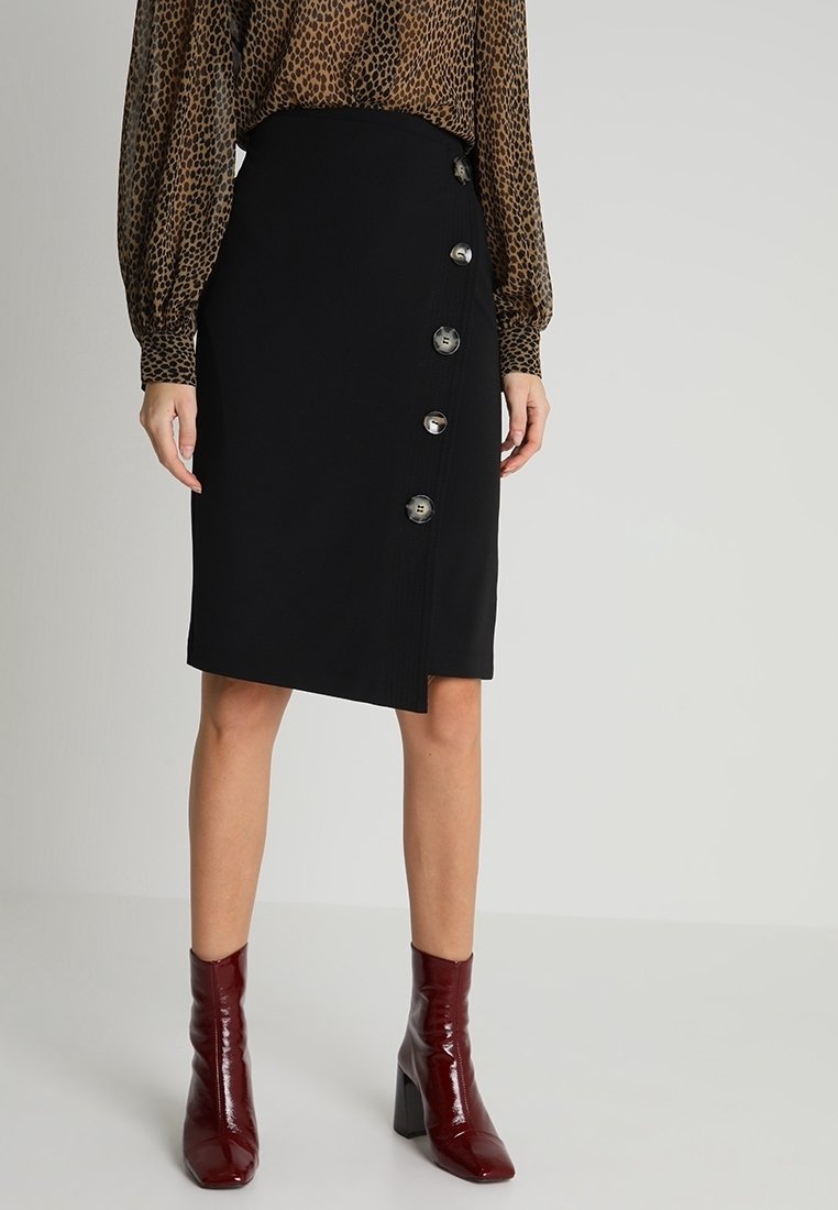 Femme portant une jupe asymétrique noire boutonnée, un chemisier à manches longues imprimé léopard, et des bottines à talons brillantes couleur bordeaux.