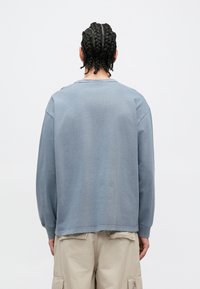 Ανοιχτό μπλε φούτερ με μακριά μανίκια, στρογγυλή λαιμόκοψη και άνετη εφαρμογή. Κατασκευασμένο από απαλό βαμβάκι με ορατές ραφές στην πλάτη.