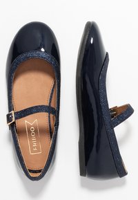 Granatowe lakierowane buty typu Mary Jane z błyszczącym paskiem, okrągłym noskiem i płaską podeszwą. Posiadają złotą klamrę i gładką podszewkę.