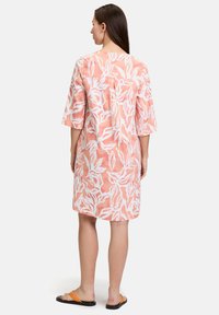 Rosa und weiße bedruckte Kleid mit lockerer Passform, knielang und mit Dreiviertelärmeln, das ein Blattmuster und eine weiche Textur aufweist.