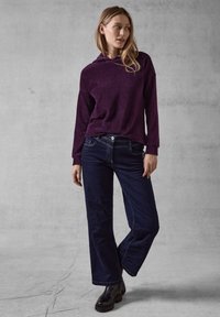 Hoodie viola a coste con cappuccio, abbinato a jeans larghi blu scuro. Stivali neri chunky completano l'outfit. Look semplice e casual.