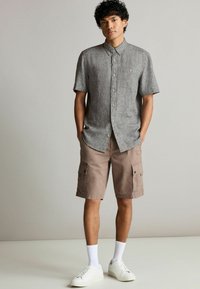 Kortærmet grå skjorte med knapper og en struktureret vævning, parret med lysebrune cargo shorts med sidelommer. Hvide sneakers fuldender looket.