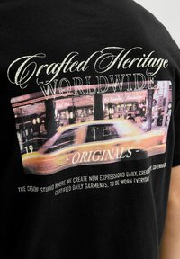 Czarny t-shirt z grafiką żółtej taksówki na tle miejskiego krajobrazu, z napisem "Crafted Heritage Worldwide" w białym i złotym kolorze.