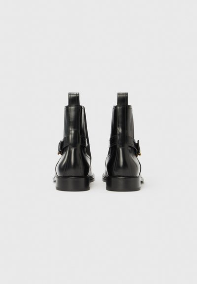 Černé kotníkové boty z hladké kůže, s boční páskem a přezkou, zaoblenou špičkou a nízkým, pevným podpatkem.