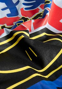 Bandiera di tessuto con un design audace in blu e rosso con accenti neri e gialli, che presenta motivi intricati su una texture liscia.