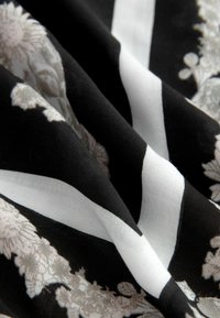 Kangasan berpola bunga dengan latar belakang hitam, yang menampilkan garis-garis putih. Teksturnya tampak halus dan desainnya mencakup warna-warna lembut.