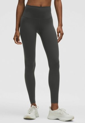 High-waisted, dark gray leggings with a smooth, stretchy texture. Paired with white athletic shoes and a simple design.