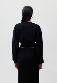 Svart kortermet genser med vide ermer og ribbestrikket søm, sammen med et matchende svart skjørt. Glatt tekstur; minimalisk design.