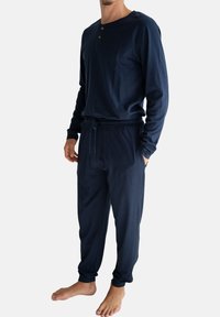 Marineblauw pyjamapak met lange mouwen, gemaakt van zachte stof. Heeft een Henley-hals met drie knopen en een elastische tailleband met een trekkoord.