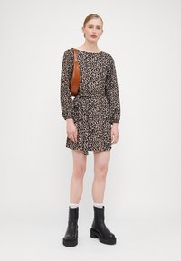 Kjole med leopardmønster, lange ermer, samlet midje og kne-lengde. Kombinert med svarte sko med tykk hæl og en brun skulderveske.
