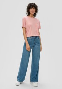 Lichtroze katoenen t-shirt met korte mouwen en een borstzak, gecombineerd met wijde blauwe spijkerbroek en witte platform sneakers.