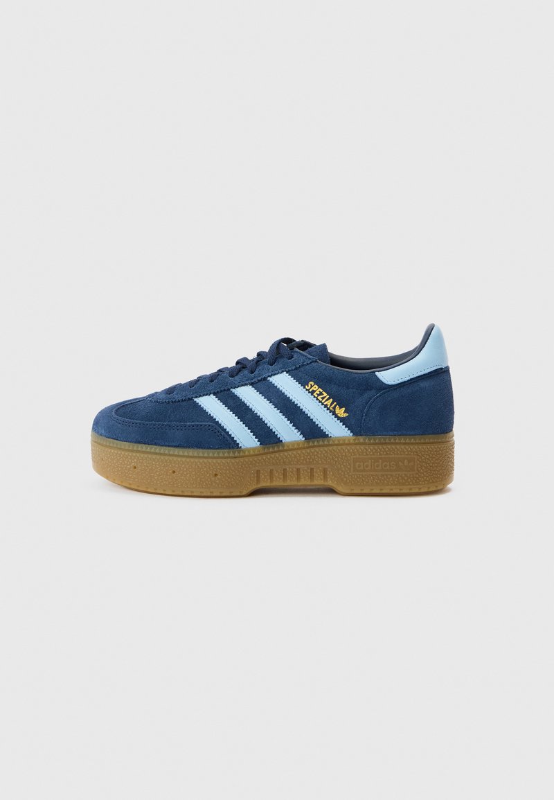 Tênis de camurça azul-marinho com riscas azul claro, biqueira redonda e sola em borracha cor de goma. Logótipo dourado "Spezial" na lateral, design clássico da Adidas.