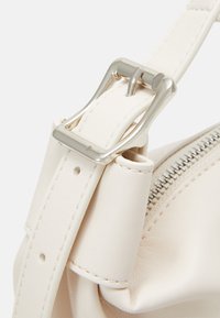 Cream leather handbag strap with silver buckle, featuring a zipper detail and smooth texture, highlighting stitching and hardware accents.