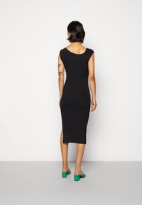 Vestido midi preto com padrão canelado, gola redonda, mangas bufantes e fendas laterais, combinado com sandálias verde de salto bloco.