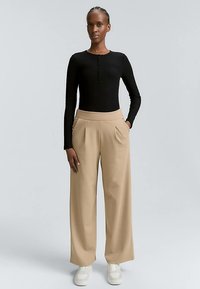 Bluză neagră cu mâneci lungi, cu dungi și închidere cu nasturi, asortată cu pantaloni bej, largi, cu talie înaltă și adidași albi. Design simplu, fără modele.