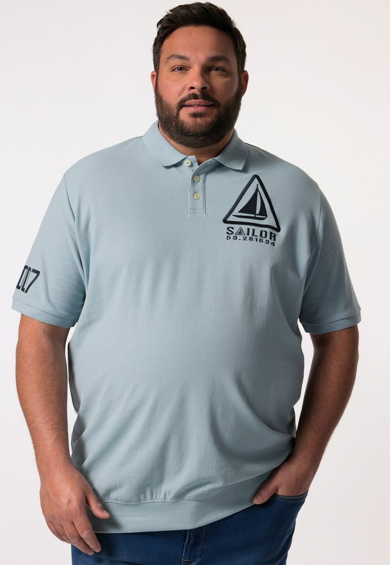 Svetle modré polo tričko vyrobené z texturované látky, s grafikou plachetnice a textem "SAILOR". Krátké rukávy se detailem "007" na levém rukávu.