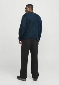 Dunkelblauer Strickpullover mit lockerer Passform, langen Ärmeln und einem etwas längeren Rückenabschluss, kombiniert mit schwarzen Hosen und Schuhen.