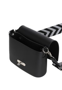 Černá syntetická kožená crossbody taška s zaobleným vrchem, stříbrným kováním a vzorovaným černobílým popruhem. Obsahuje kovové zapínání na patent. 