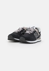Black suede sneakers with gray accents, featuring a white midsole, contrasting laces, and a textured rubber outsole. Model 574.