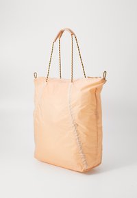 Perzikkleurige nylon schoudertas met een zachte textuur, voorzien van gouden kettingriemen en een toelopend ontwerp aan de bovenkant.
