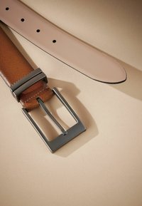 Ceinture en cuir brun avec une finition lisse, large sangle beige et boucle rectangulaire en métal argenté. Présente plusieurs trous d'ajustement.