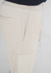 Pantalones jogger beige fabricados con una tela suave. Cuentan con una cintura elástica, bolsillos frontales y un bolsillo lateral tipo cargo con una textura suave.