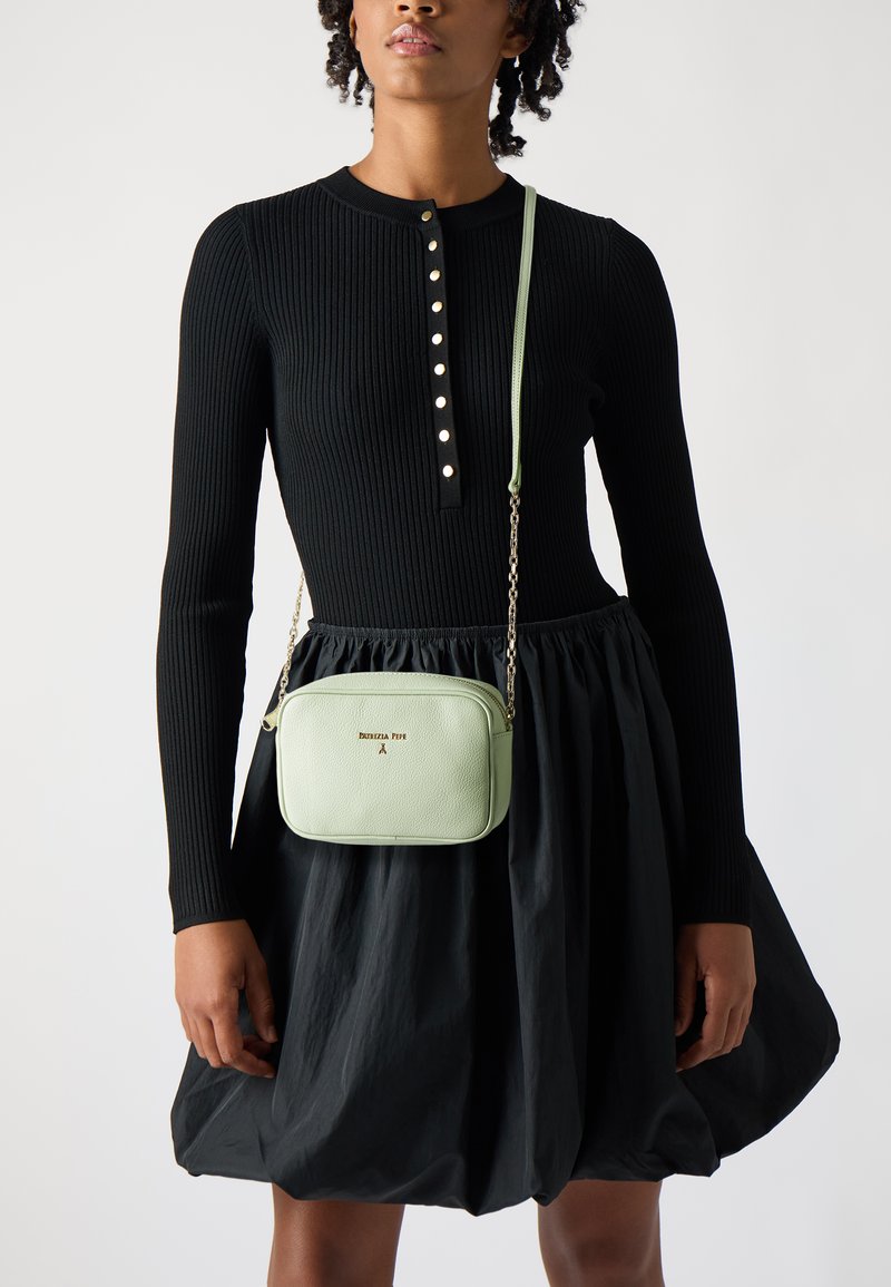 Top nero a coste a maniche lunghe con pattina dei bottoni, abbinato a una gonna nera a campana. Presenta una borsa a tracolla rettangolare verde menta con tracolla a catena.