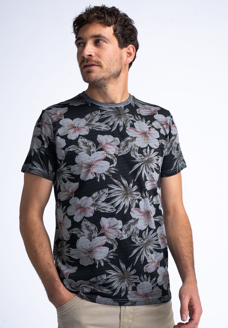 Camiseta negra con un vibrante patrón floral que incluye hibiscos y hojas tropicales. Cuello redondo, mangas cortas y textura suave.