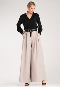 Czarna bluzka z długim rękawem i dekoltem w serek, zestawiona z jasnobeżowymi spodniami o szerokich nogawkach. Posiada czarny pasek z okrągłą klamrą, prosty i elegancki design.