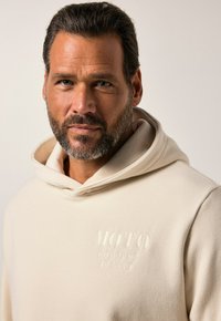 Sudadera beige claro con un logo bordado plano que dice "MOTO COMPANY JP 1880". Cuenta con una capucha con cordón y un tejido suave y texturizado.