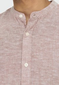 Camicia di lino rosa chiaro con colletto alla mandarino, dotata di una patta con due bottoni e una delicata texture su tutto il tessuto.