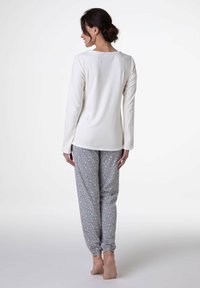 Maglietta crema a maniche lunghe con scollo arrotondato e pantaloni del pigiama grigi con motivi piccoli floreali e polsini elastici.