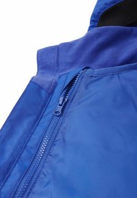 Nahaufnahme eines teilweise geöffneten Reißverschlusses einer blauen Jacke, die Stoffstrukturen und Details der Nähte zeigt.