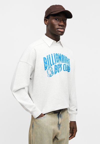 Ανοιχτό γκρι φούτερ με μπλε γραφικό "Billionaire Boys Club", λεπτομέρεια στο γιακά και χαλαρή εφαρμογή. Καφέ καπέλο, ανοιχτόχρωμο τζιν με κάθετες ρίγες.