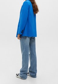 Klarblå blazer med strukturerade axlar och långa ärmar. Bärs över ljus tvättade denimjeans och matchas med svarta och vita skor.